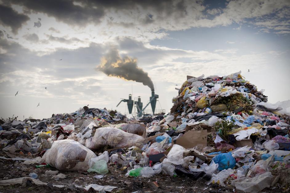 Stock photo of piles of trash in a landfill with smoke in the background. 