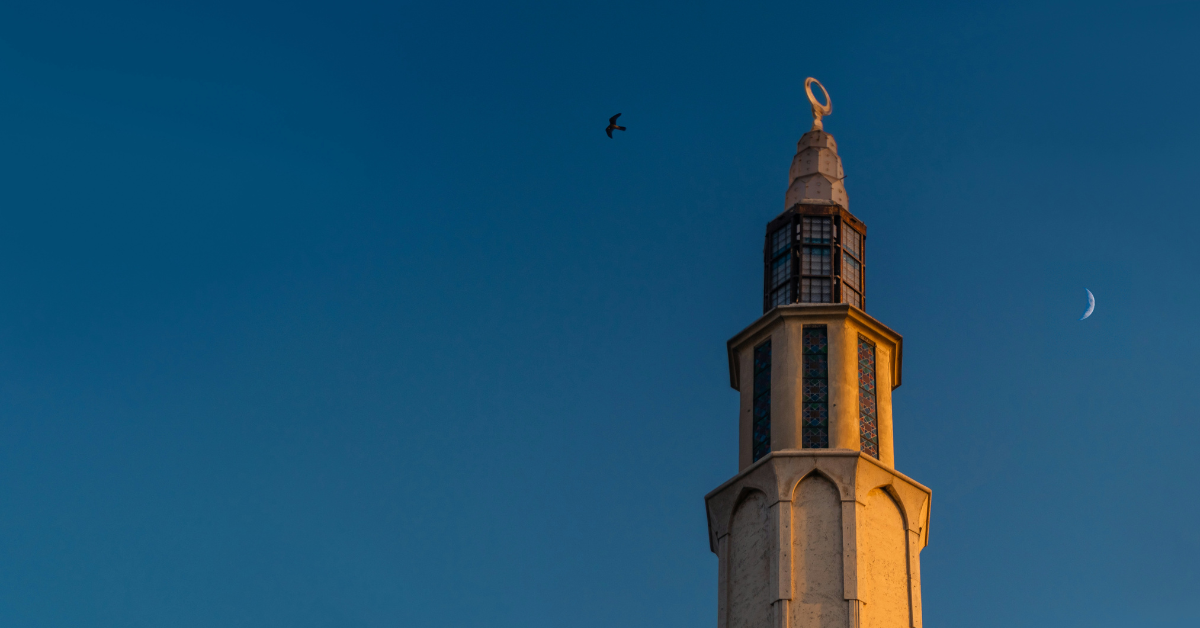 A moon hangs in the sky next to a tower