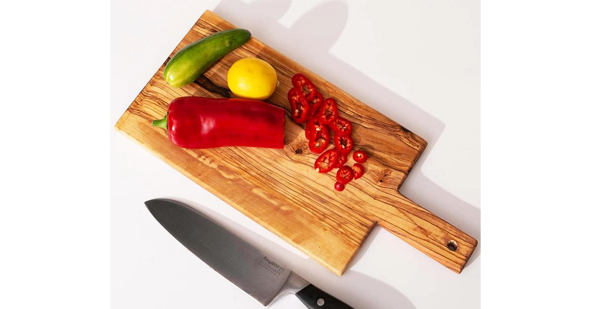 paddle-style olive wood cutting board with knife and chopped up pepper.