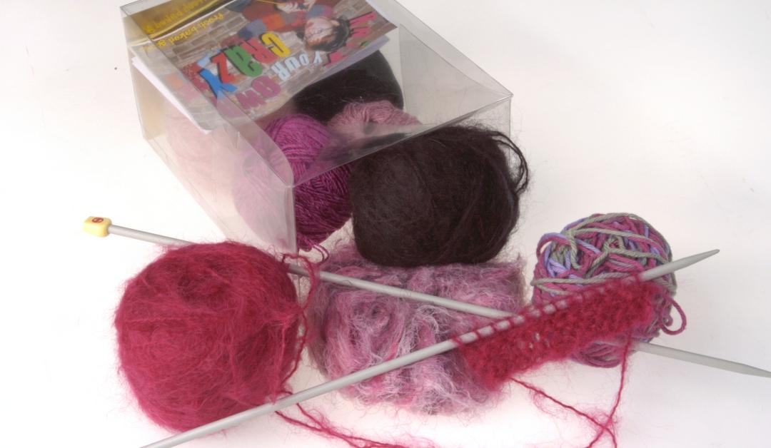 A knitting kit in a transparent box containing spools of thread and knitting needles