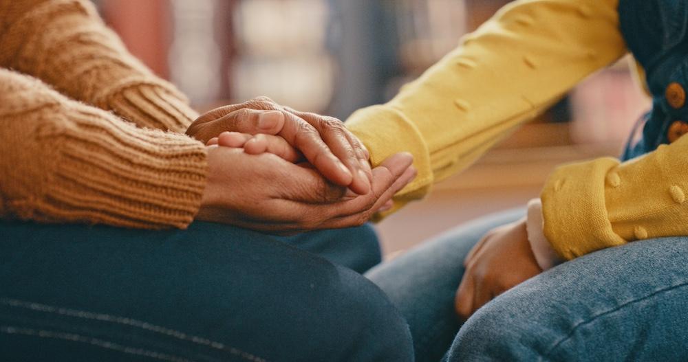 Two people holding each other's hands in support.