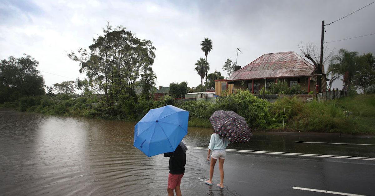 Two children hold umbrellas dip their feet in the rising floodwaters along the Hawkesbury River in the township of Windsor on March 22, 2021 in Sydney, Australia.