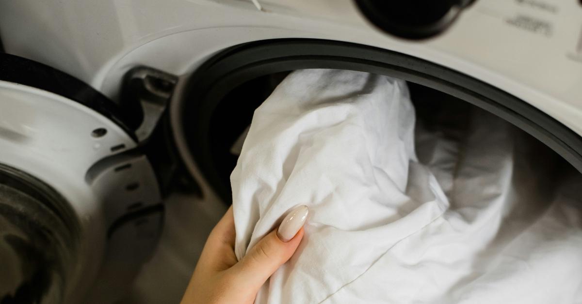 Woman puts a white piece of cloth into a dryer. 