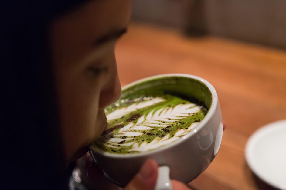 A woman drinks a matcha latte with a leaf design on the top. 