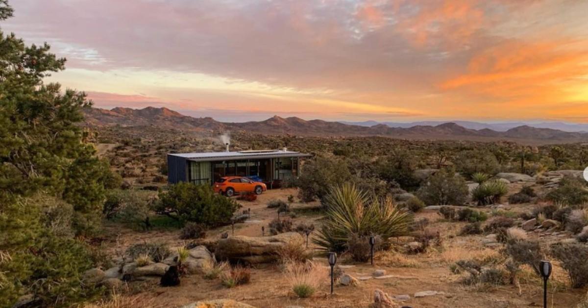 A small shipping container in the middle of the Joshua Tree desert with a stunning sunset in the background