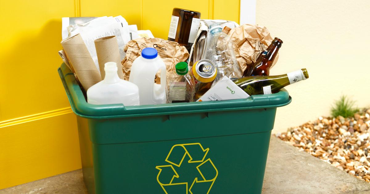 A green recycling bin filled with bottles, paper, cans, and more