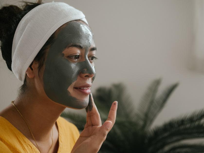 A woman with a white headband puts a green face mask on her face. 