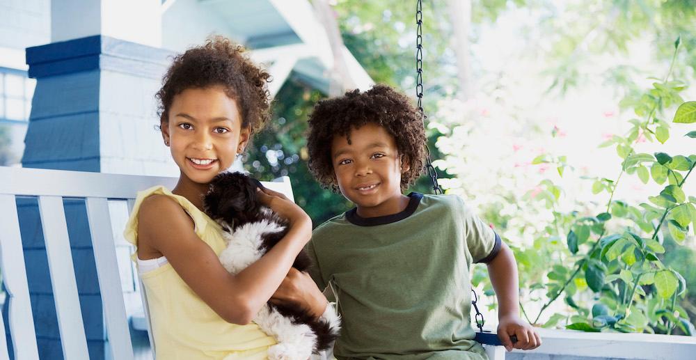 Kids holding a shih tzu on an outdoor swing. 