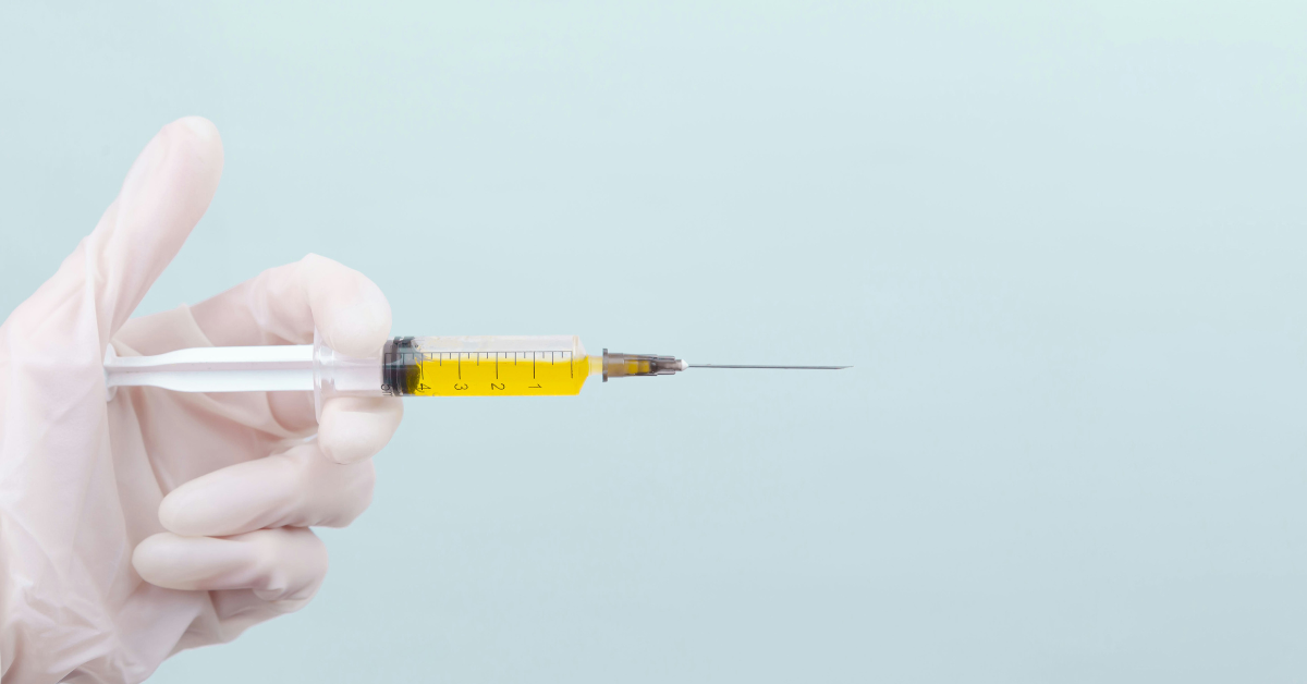A gloved hand holds a syringe of yellow liquid
