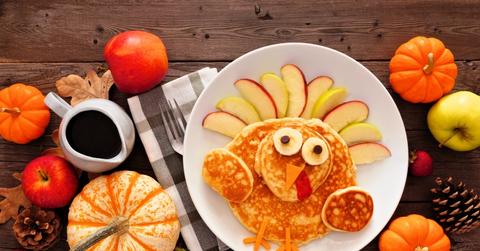 Pancakes with apple slices above them are pictured on a plate beside pumpkins of various sizes.