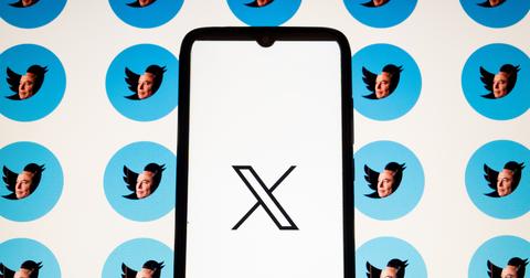 A photo of a phone screen with the X logo on the screen in from of a background of Elon Musk's face filling the Twitter bird logo.