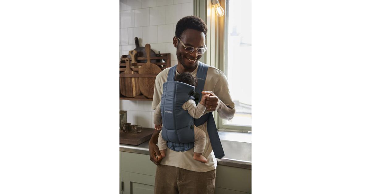 Smiling dad holding baby in blue baby carrier.