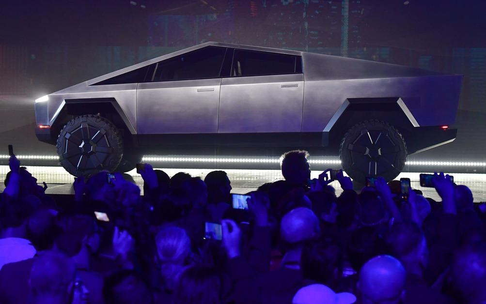 A Tesla Cybertruck sits on a stage in front of a crowd of people holding up their phones to take pictures. 