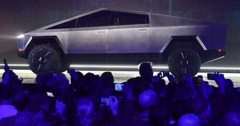 A Tesla Cybertruck sits on a stage in front of a crowd of people holding up their phones to take pictures.