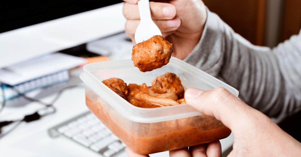 A guy eating leftover spaghetti and meatballs from a plastic container. 