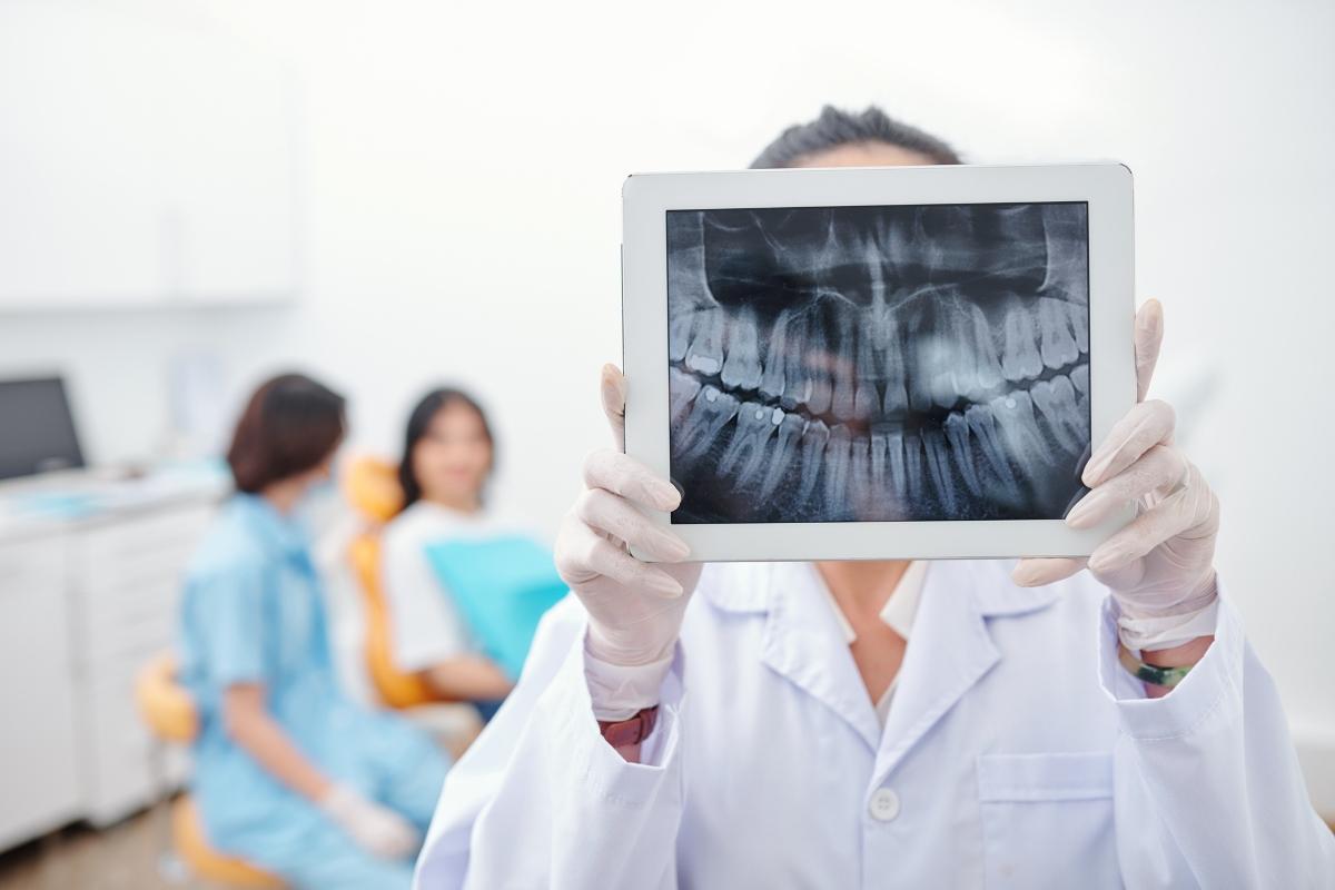 Dentist holding up x-rays on a tablet.