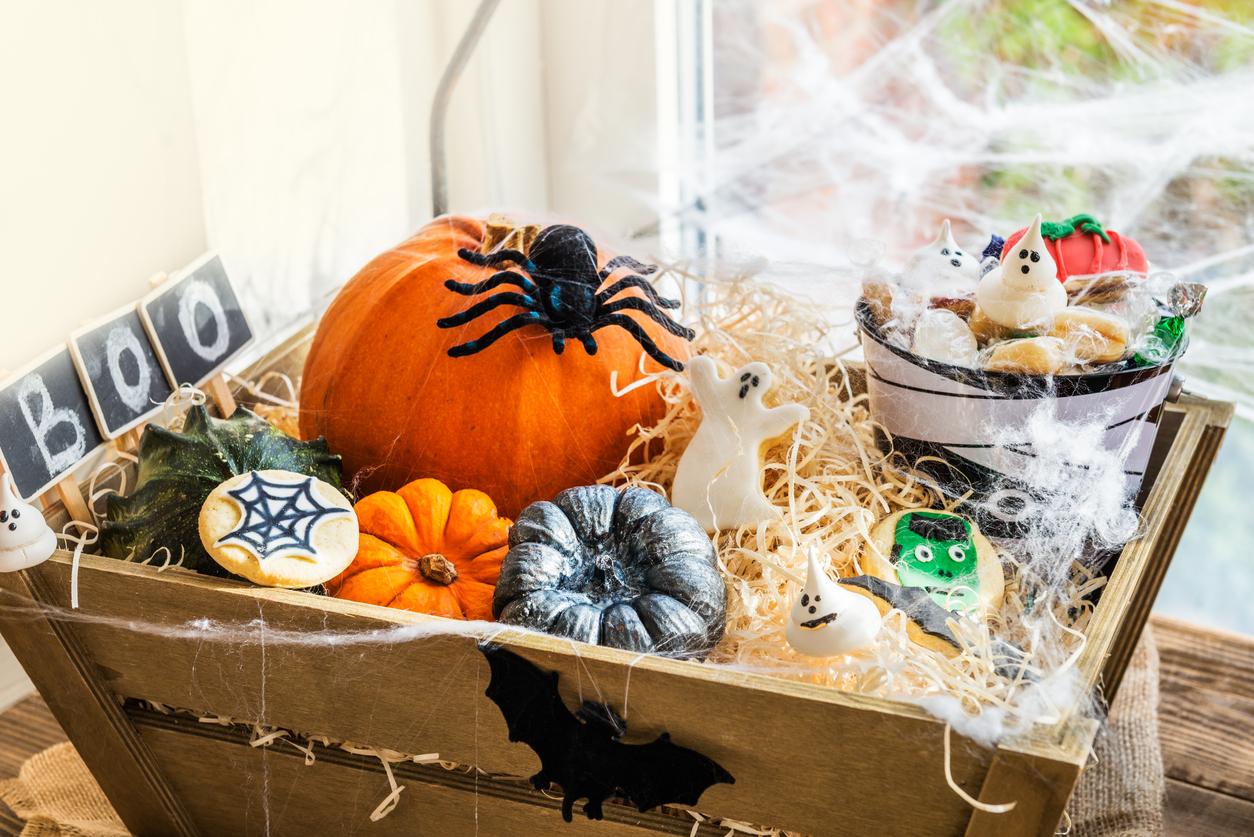 Wooden basket decorated with fake spider webs and filled with halloween treats and mini pumpkins.