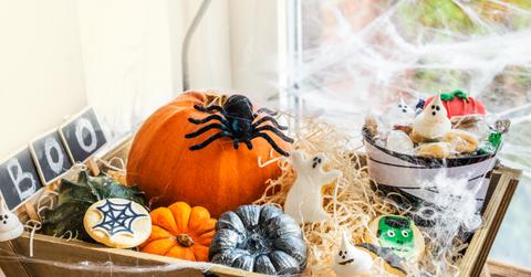 Wooden basket decorated with fake spider webs and filled with halloween treats and mini pumpkins.