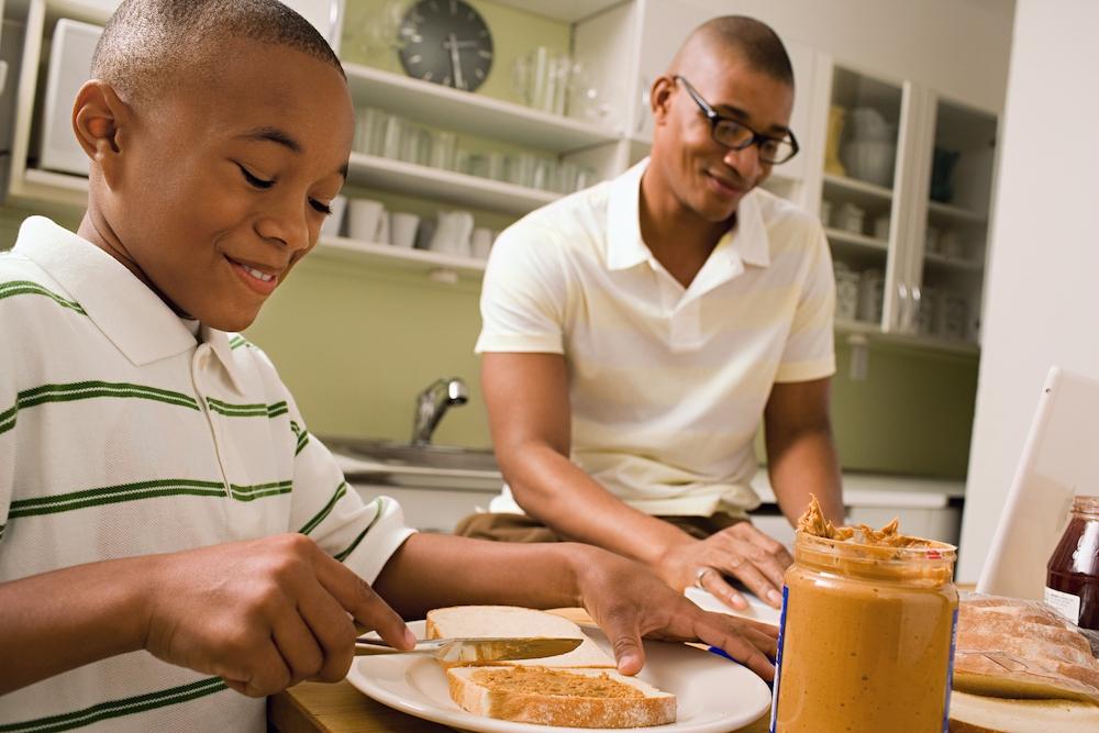 A father and son spreading peanut butter on white bread. 