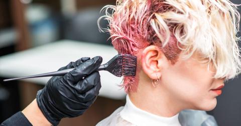 Hairdresser hand in gloves applies pink hair dye to client's bleached hair