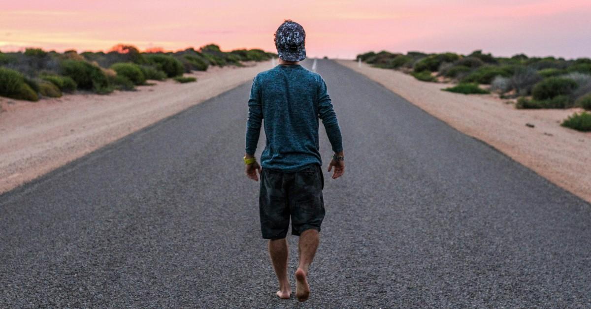 A man stands in the middle of the road in bare feet while looking towards the horizon