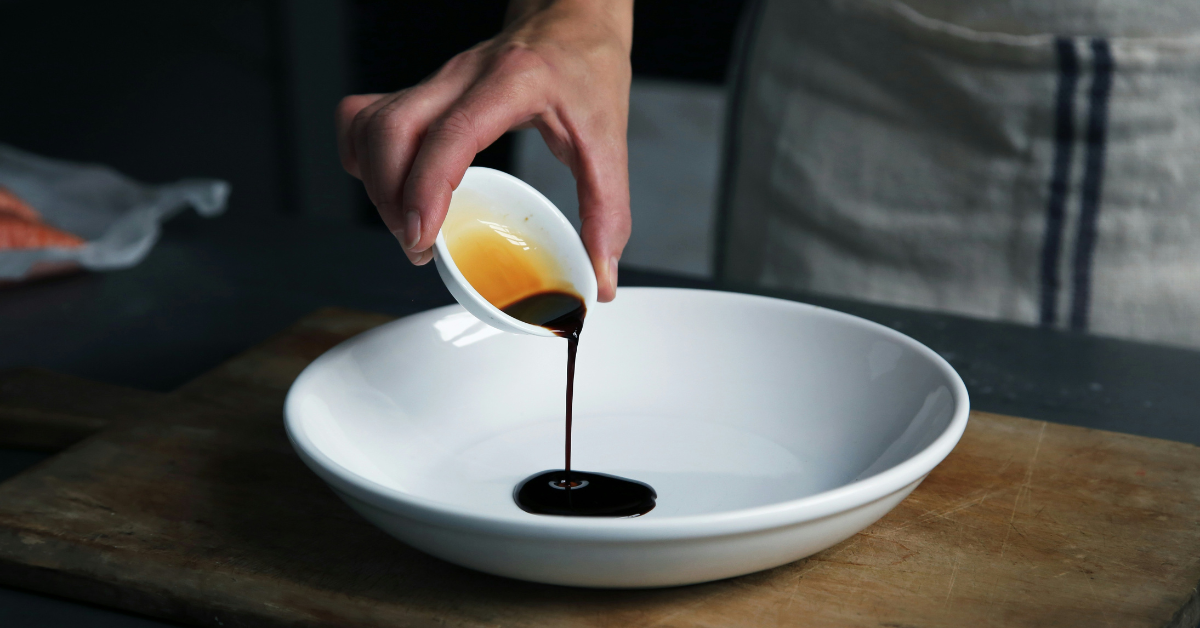 A person pours a container of balsamic vinaigrette into a bowl