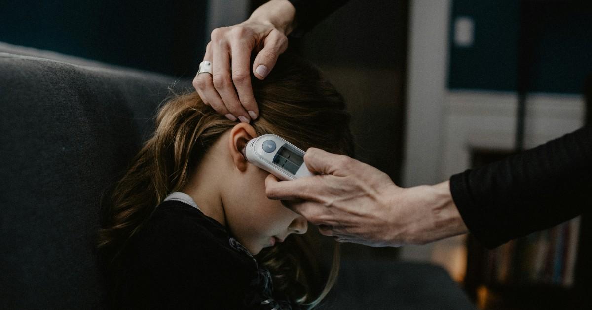 A woman takes her sick daughter's temperature through her ear 