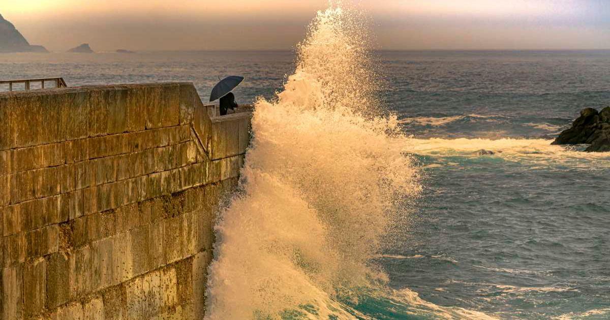 A lady with an umbrella protects herself from a giant wave. (Representative Cover Image Source: Getty Images | Andrés Pérez Wittmann)