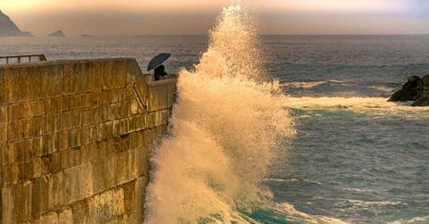 A lady with an umbrella protects herself from a giant wave. (Representative Cover Image Source: Getty Images | Andrés Pérez Wittmann)