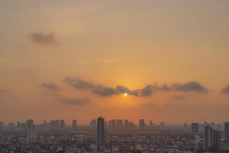 A photo of downtown Bangkok during sunset, where the buildings are blanketed with a heavy smog. 