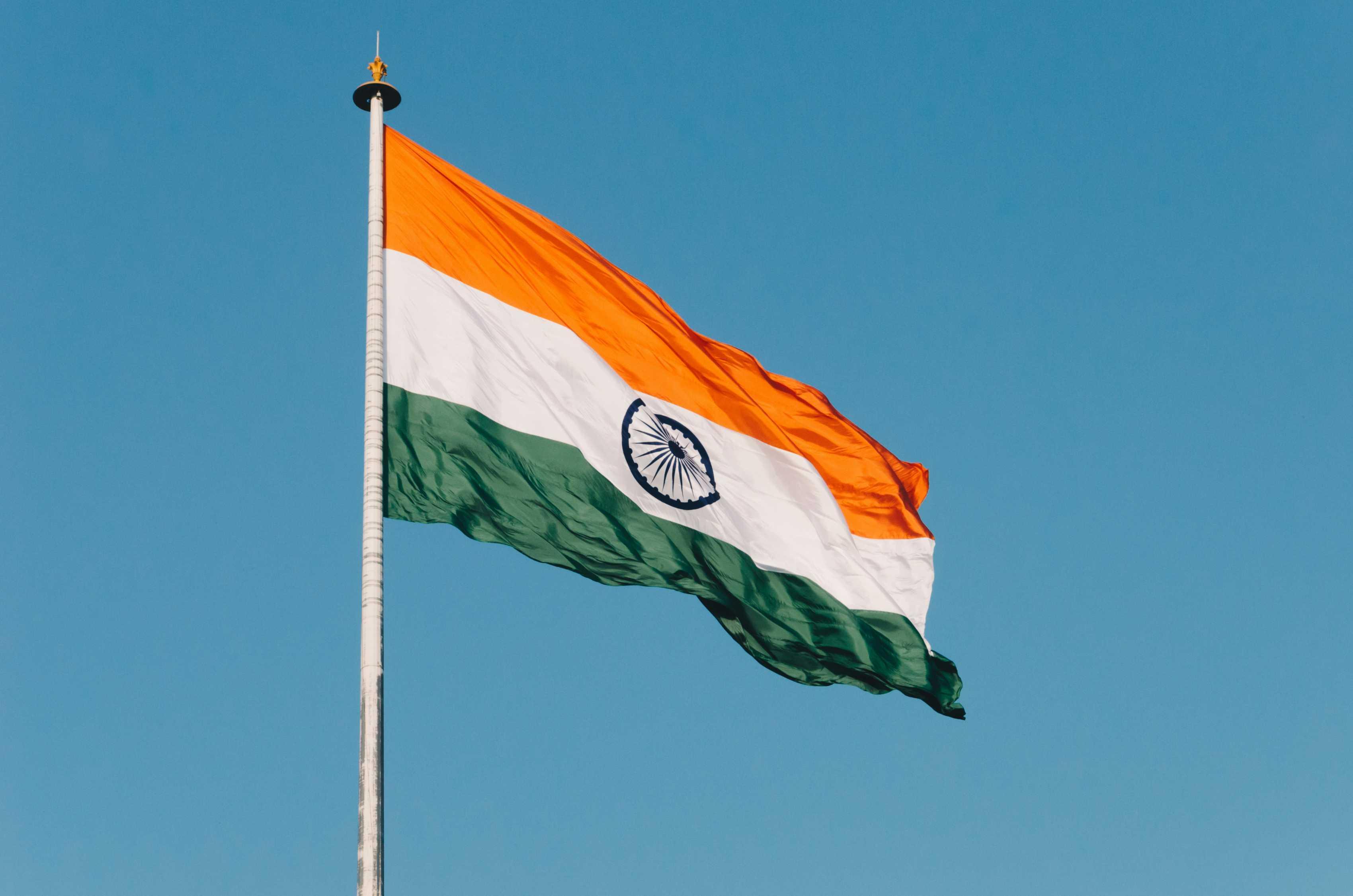 The flag of India is pictured waving on a pole against a clear blue sky.