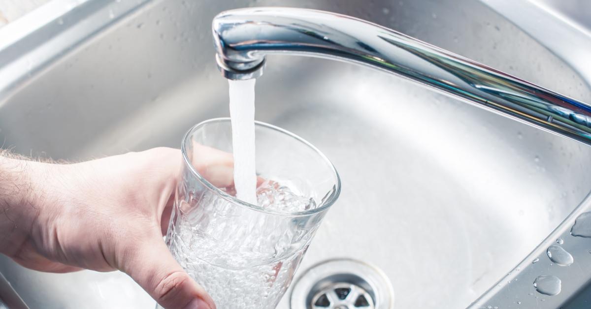 Hand holding glass under running kitchen faucet. 