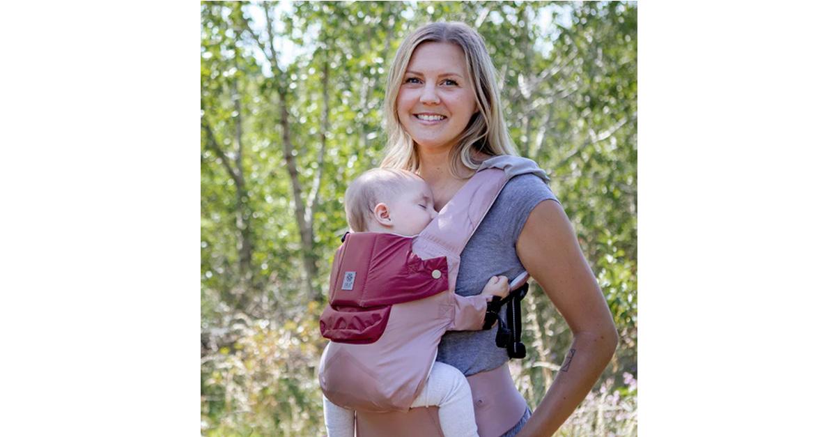 Smiling woman carrying sleeping baby in pink baby carrier