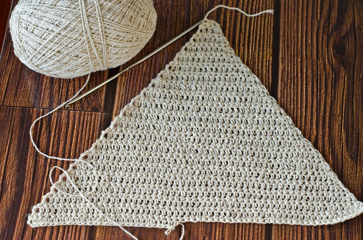 A white crochet triangle on a dark wood table.