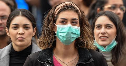 A woman wears a medical mask, with several other people standing behind her.