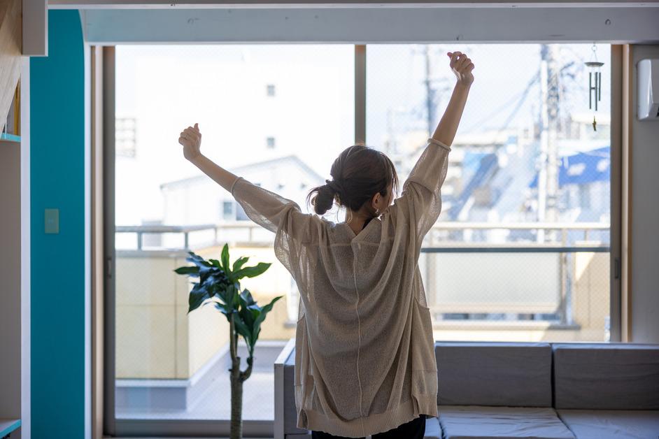 Women stands in front of a window while stretching her arms up towards the ceiling. 