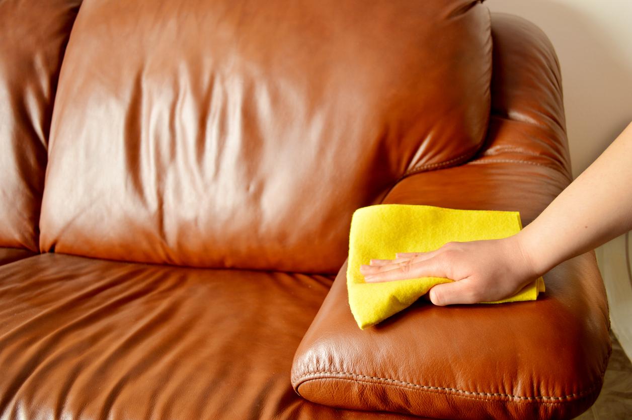 A person's hand using a yellow cloth to wipe down a leather couch.