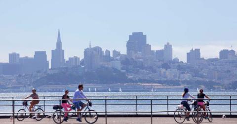 People riding bicycles on a pier with the San Francisco city skyline in the background. (Cover Image Source: Getty Images | Grant Faint)