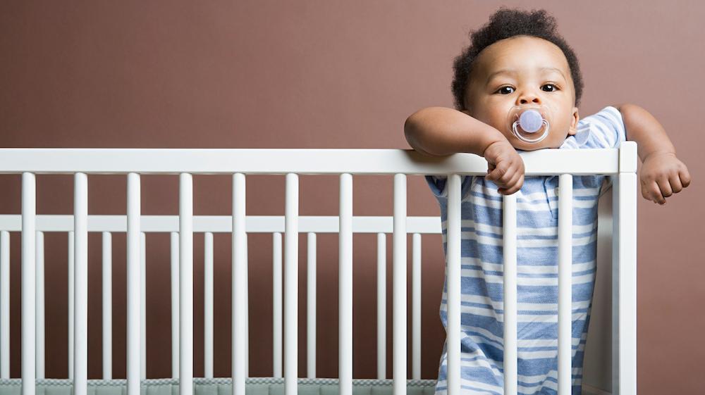 A baby standing in a crib.