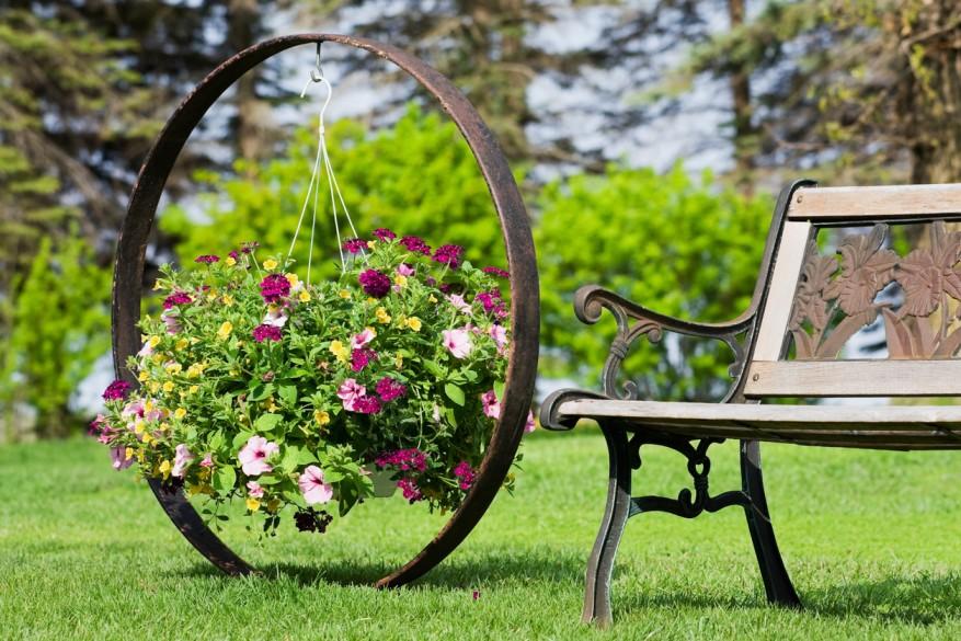 Wooden bench next to an iron hanging plant holder with pink and yellow flowers. 