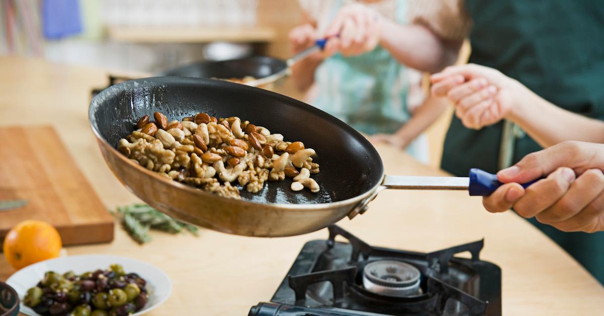 A hand roasts nuts on non-stick cookware