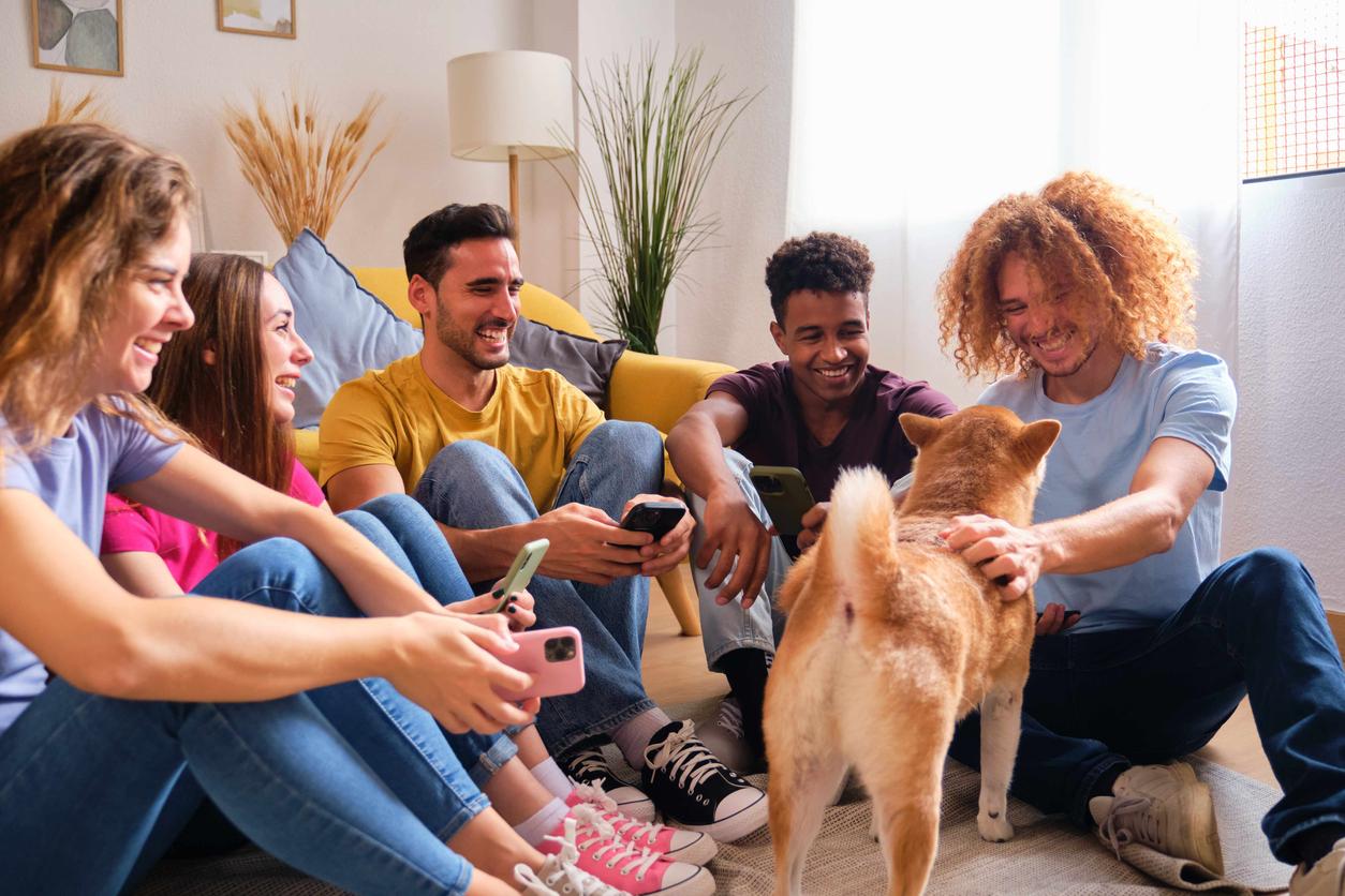 A group of friends in a living room smile while petting a dog.