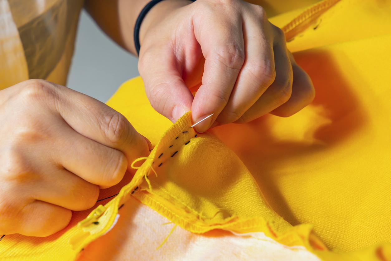 A close up view of someone hand sewing yellow fabric.