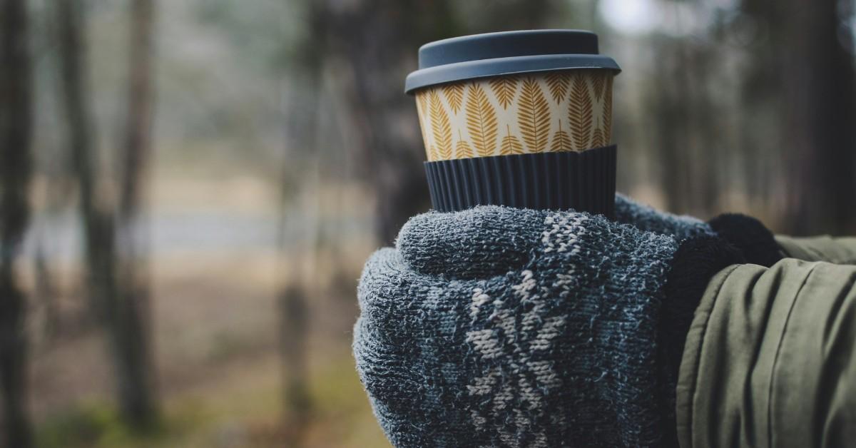 A pair of gloved hands holds a cup of warm coffee