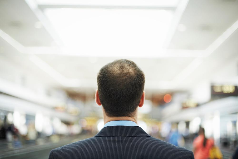 A balding man looking away from the camera is in a suit. 