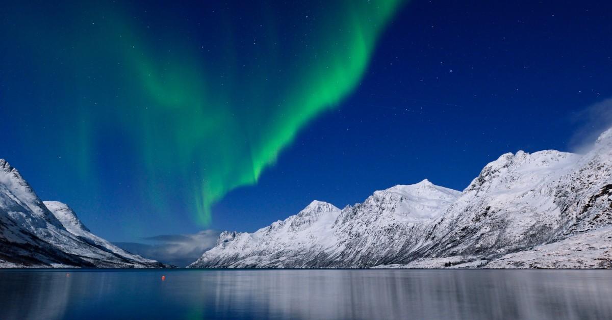 A green aurora is visible over the snowy mountains and water