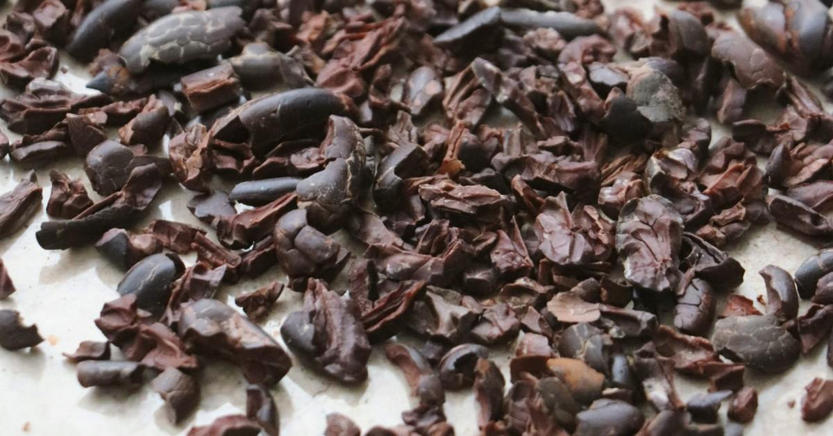 Whole cacao beans and nibs lay on a white countertop