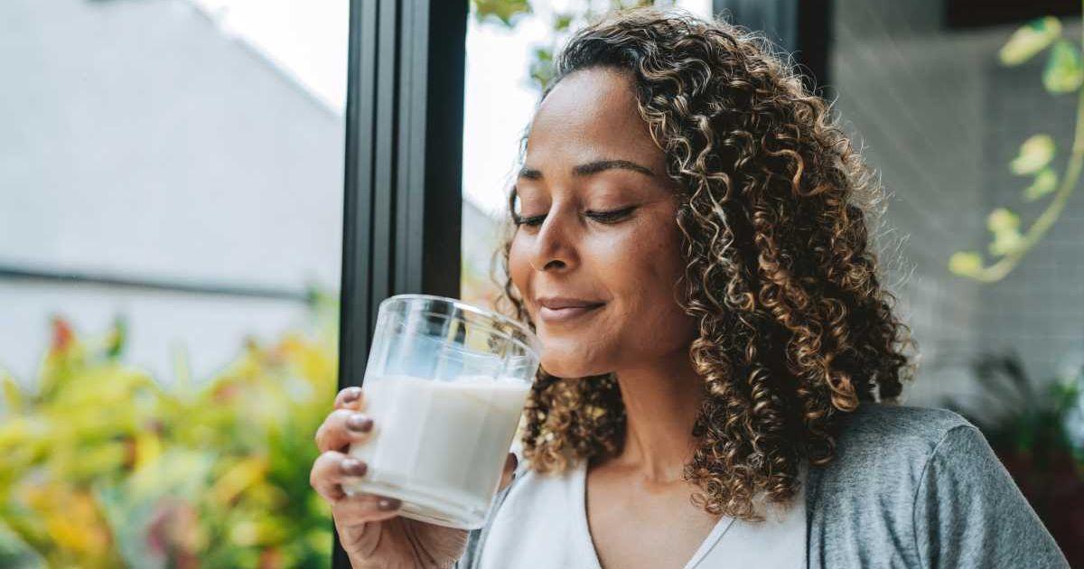 Woman drinking from a glass of milk while standing beside a window (Representative Cover Image Source: Getty Images | AndresWD)