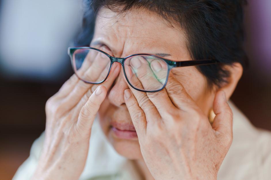 Older woman with short dark hair rubs her fingers on her eyes under her glasses. 