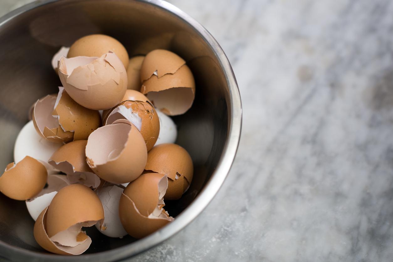 A group of cracked brown egg shells remain in a metal bowl on a marble countertop.